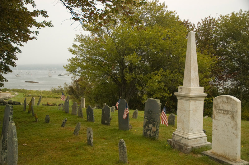 Waters of a bay can be seen beyond a row of tombstones.