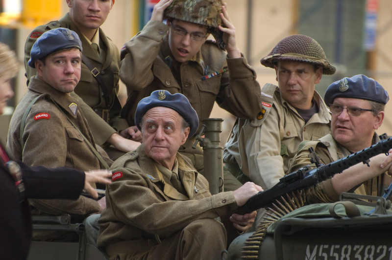 Six men in World War II garb sit on a jeep with a machine gun.