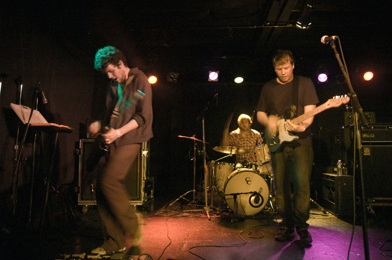 Two guitarists and a drummer, on a small stage.