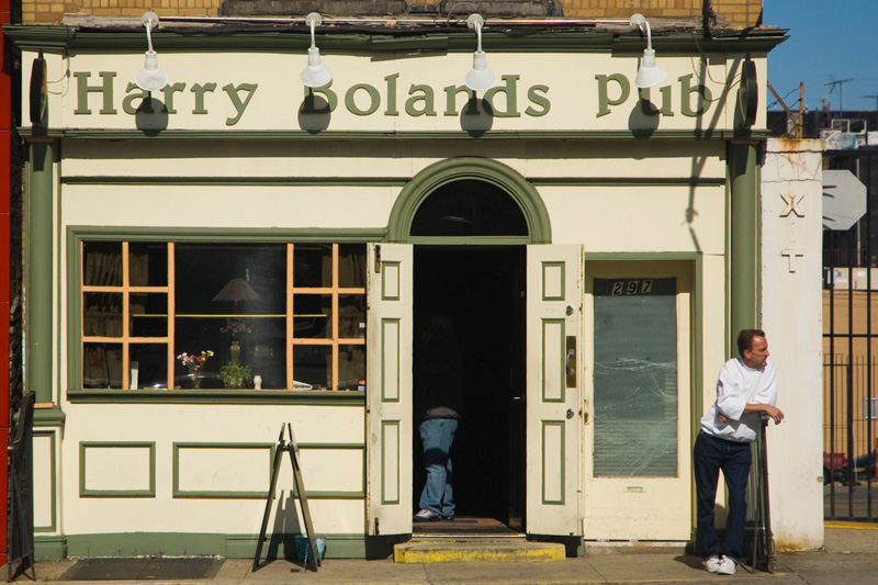 Outside the open door of a pub, a patron leans on a fence.