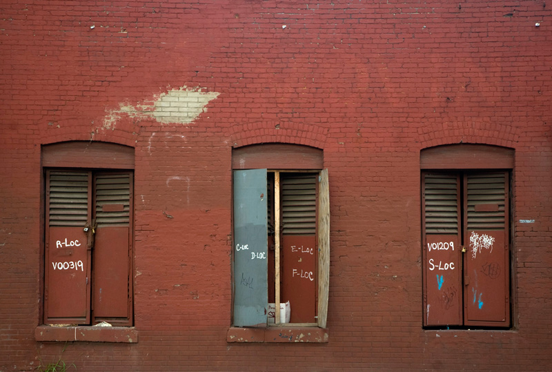 Three windows in a red brick wall have been closed up with louvered gates.