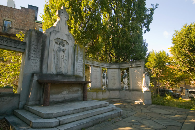 An outdoor altar is built into a wall decorated with statues and engraved with saints' names.