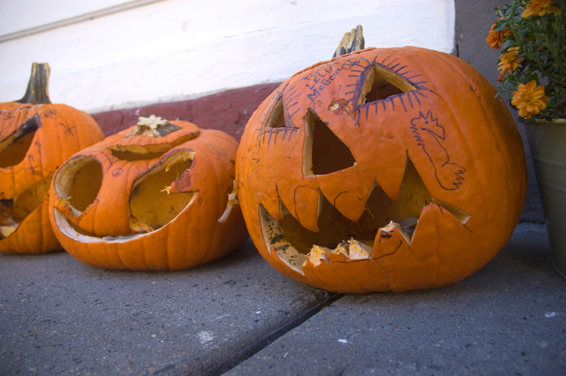 Three carved pumkins on a sidewalk, worn out from their candles.