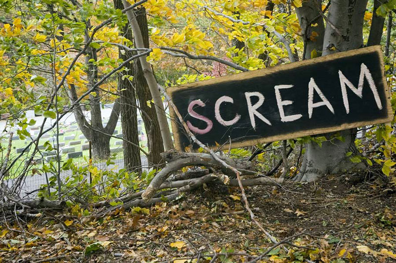Next to a cemetery, a sign encourages kids to SCREAM for Halloween.