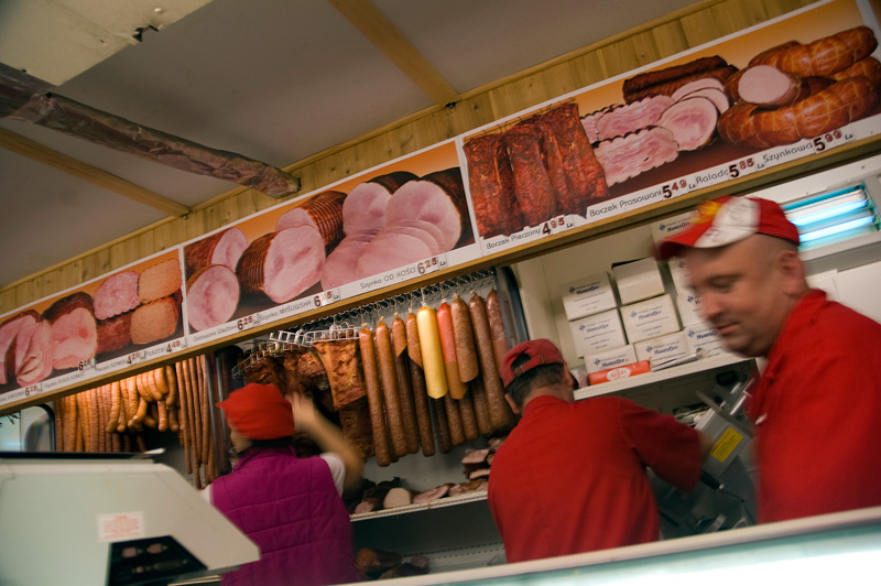 Three people in red uniforms slice meat, select sausages, and so on.