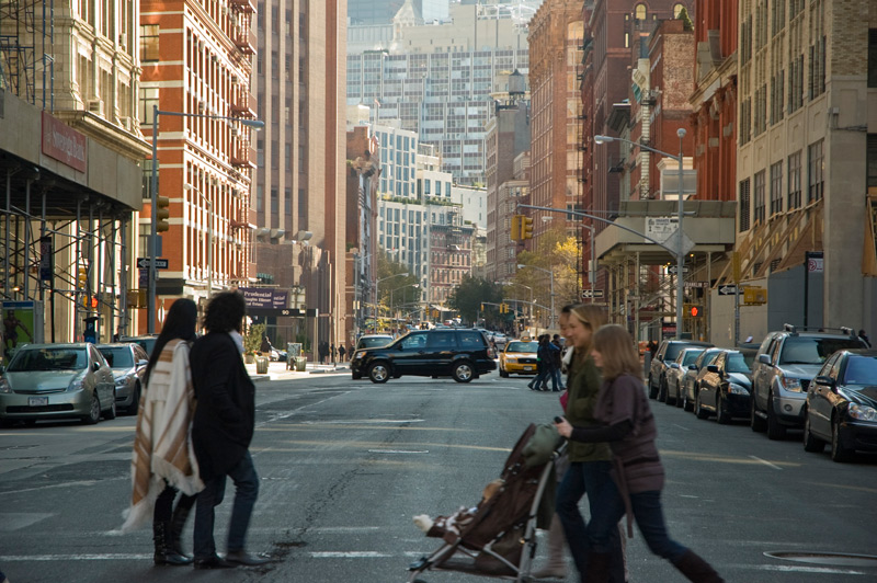 Families cross from opposite sides of the street, with skyscrapers in the distance.