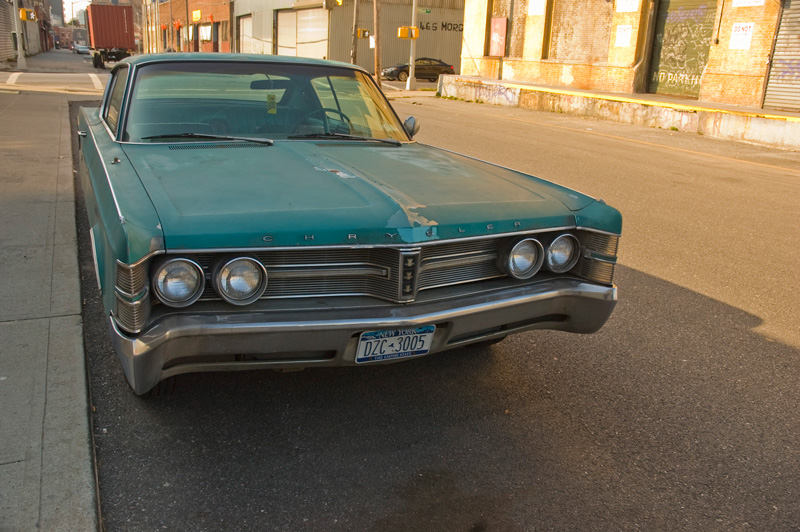 A large old Chrysler, worse for the wear, parked on an empty industrial street.