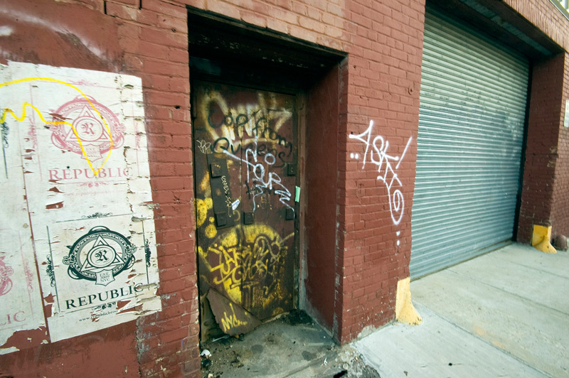 A metal door on a brick building, spray-painted with graffiti.