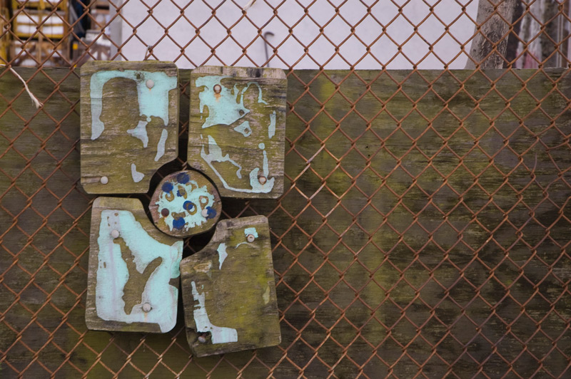 Decorated wooden panels have been bolted to chain link fence.