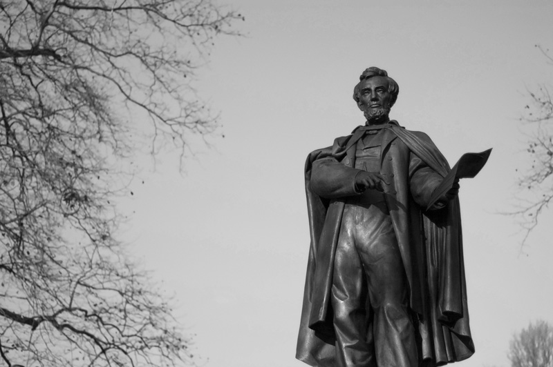 A statue of Abraham Lincoln, cloaked, in a clearing of trees.