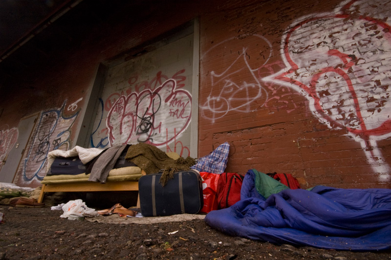 A small suitcase, blankets, and a sleeping bag lie next to a loading dock.