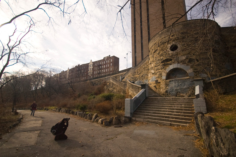 A photographer squats to take a picture of a stone structure.