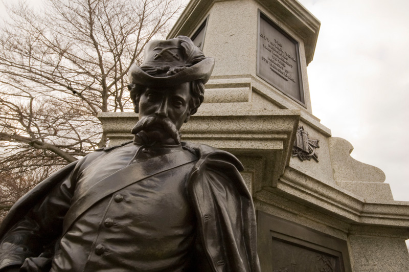 Statue of a civil war soldier, with head low, in front of a pedestal.