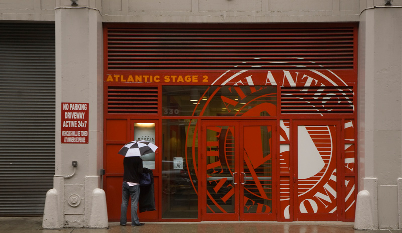 A man in black and white clothing, with a black and white umbrella, in fromt of red doors.