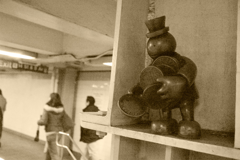 A cartoonish sculpture of a tiny man gathering huge pennies.