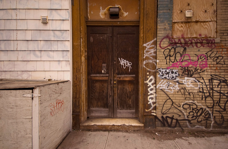 Graffiti covers the brick wall next to a wooden door.