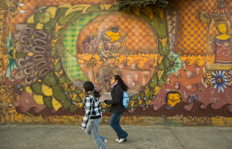 Two people trot past a brilliant, fanstastic mural.