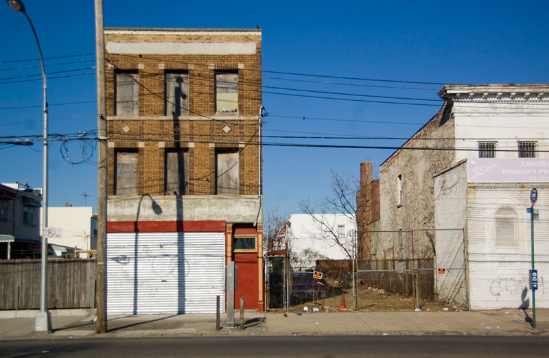 A short, boarded-up building between two empty lots.