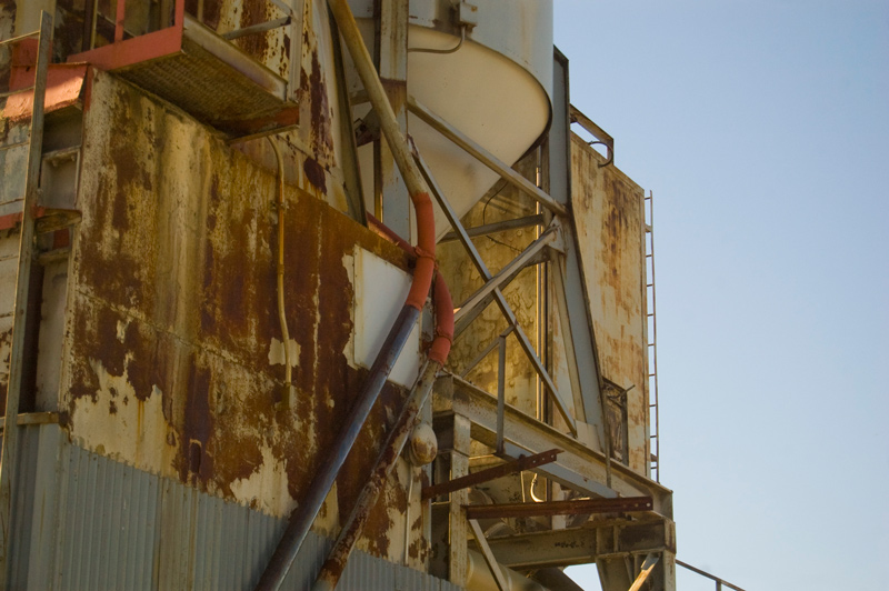 Rusted metal of a cement factory hopper, against a blue sky.