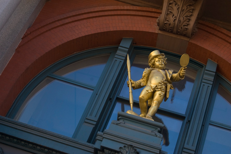 A gilded statue of Puck holds pen and gazes at his reflection.