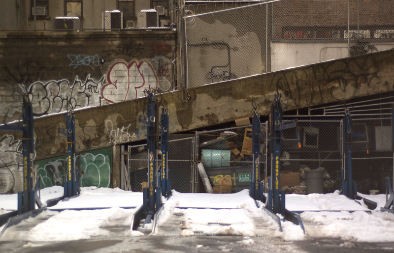 Snow covers asphalt and parking hoists in a parking lot.