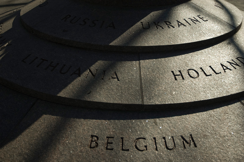 Shadows obscure the engraved names of nations on a pedestal.