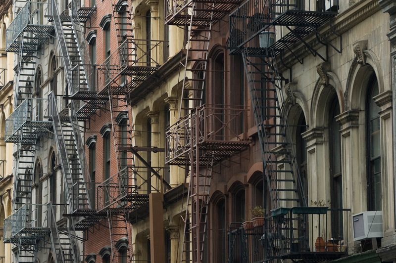 A row of different styled, different colored buildings, with fire escapes on the front.