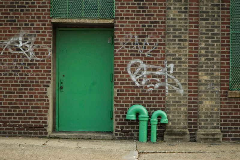 A brick industrial building with a green door and green pipes.