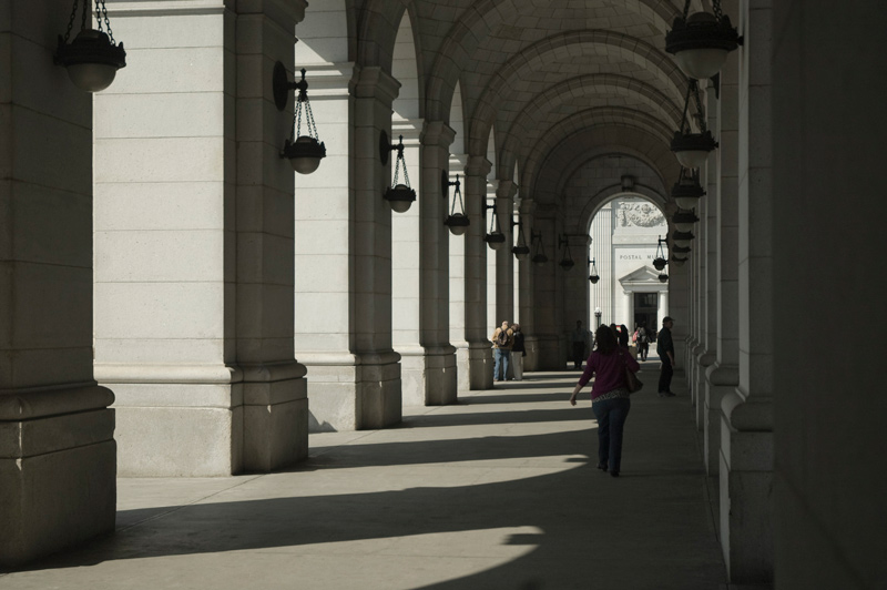 A long hallway filled with shadows from columns and light from their gaps.