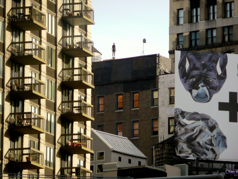 A statue of a naked man on the edge of a building.