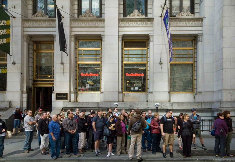 A sidewalk in front of an ornate building is filled with a walking tour group.