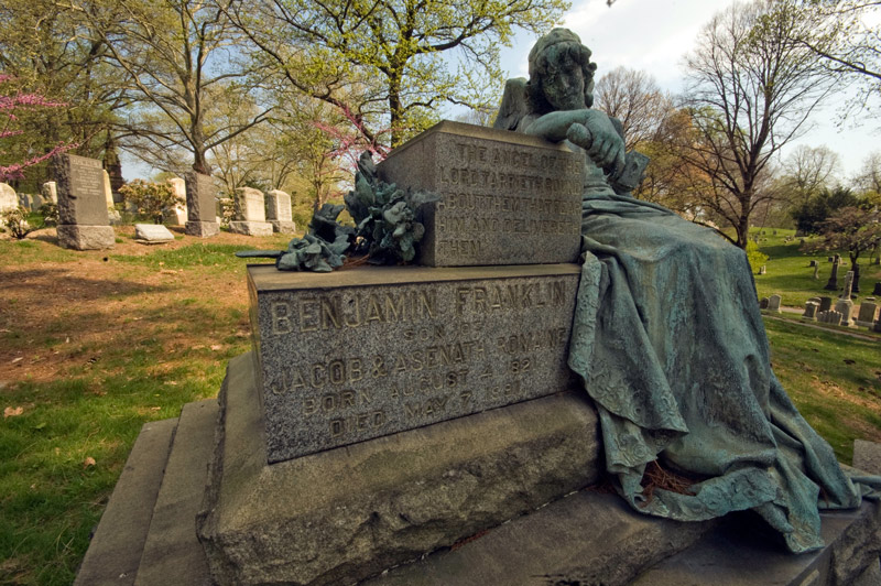 An angel reclining by a tomb, having chiseled the name of the deceased.