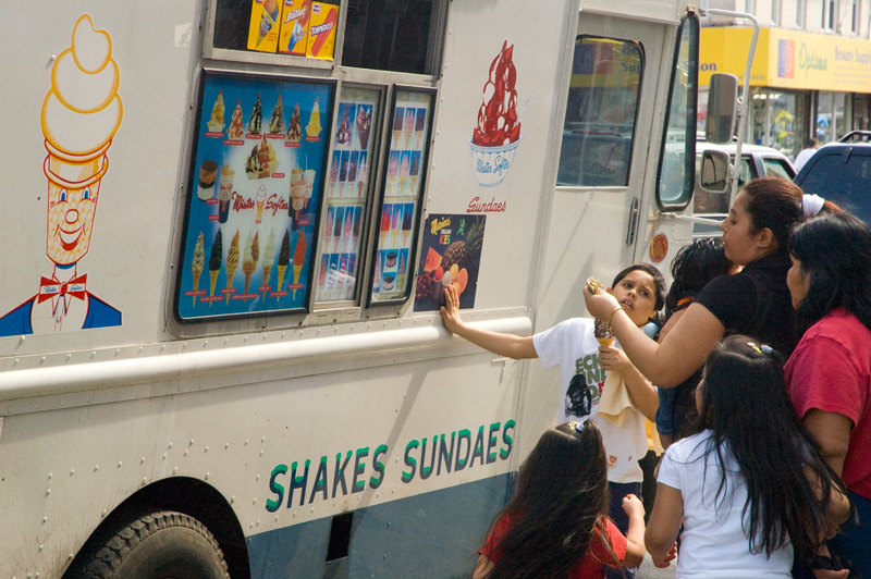 A mother hands money to an ice cream vendor in a truck.