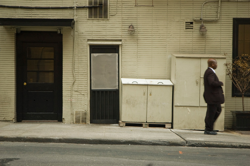 A man in a suit, walking past doors and sanitation cabinets.