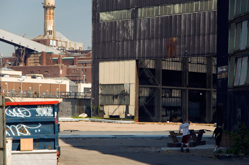 Two kids play in the shadows of an industrial expanse.