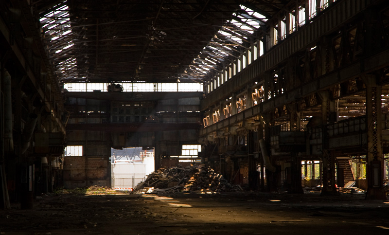 Sun shines through high windows in a dark empty building.