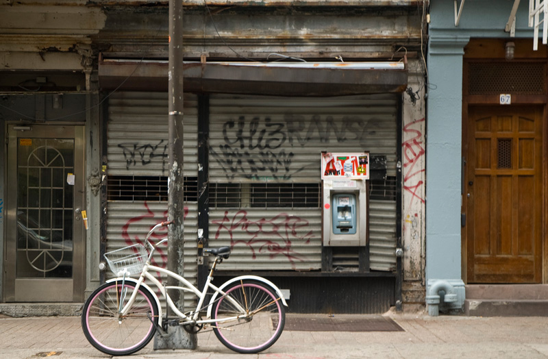 A white bicycle in front of a store, whose rolled down front has graffiti on it.