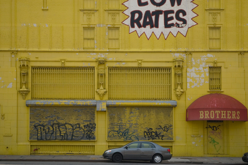 A huge yellow building, with a car parked in front.