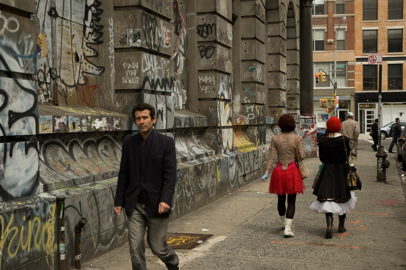 Two women, one in a red skirt and the other in a red hat, on a block with graffiti.