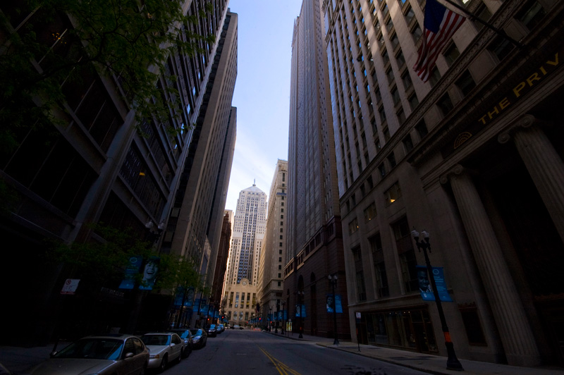 A dark canyon of buildings, with a building at the end, in light.