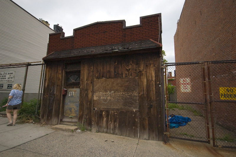 A woman on her phone walks past a brown, wooden shack.