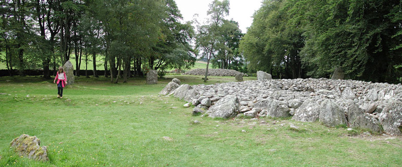 A child walks past cairns in a green field.