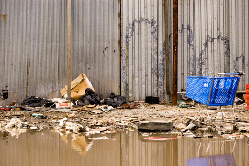 A blue shopping cart, among rubble and pooled muddy water.