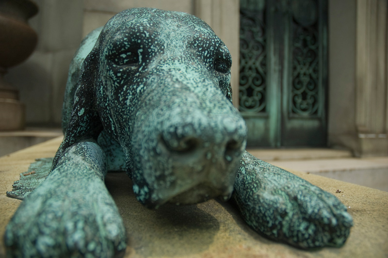 A bronze dog lies outside a mausoleum.