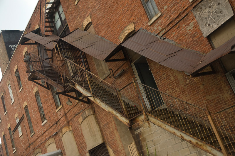 A rusty metal staircase on the side of an industrial building.