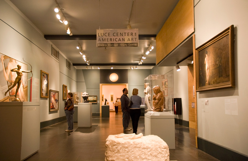 A few people look at sculptures and paintings in a museum gallery.