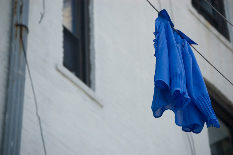 A lone, blue blouse, hanging on a clothes line.