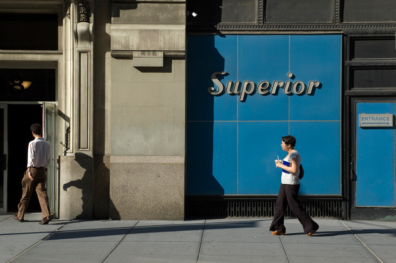 People pass a blue building front, marked with the word 'Superior.'