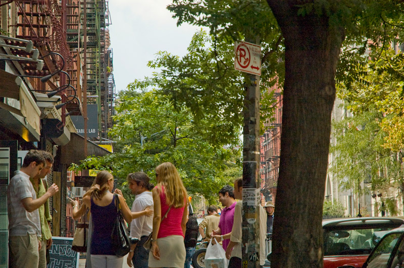 People clustered outside a restaurant early on a summer afternoon.