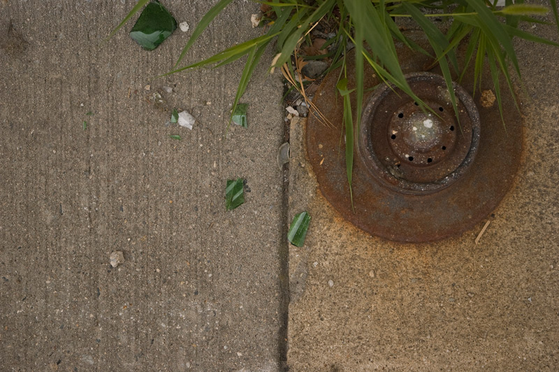 Separate parts of a sidewalk, with broken glass and weeds.